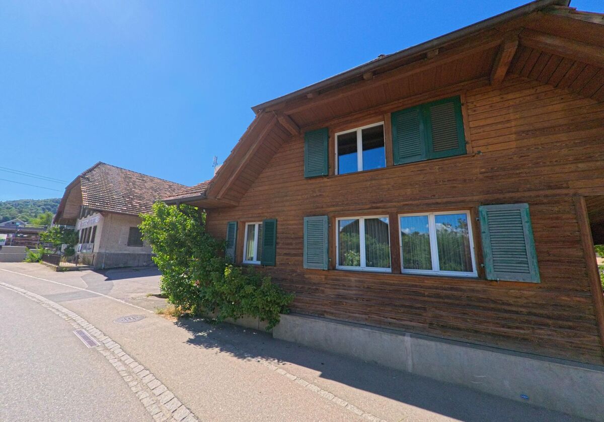 In Thurnen (3127, Kanton Bern) stehen zwei traditionelle Wohnhäuser mit Holzfassade und grünen Fensterläden an einer leicht geschwungenen Strasse im Ortskern.