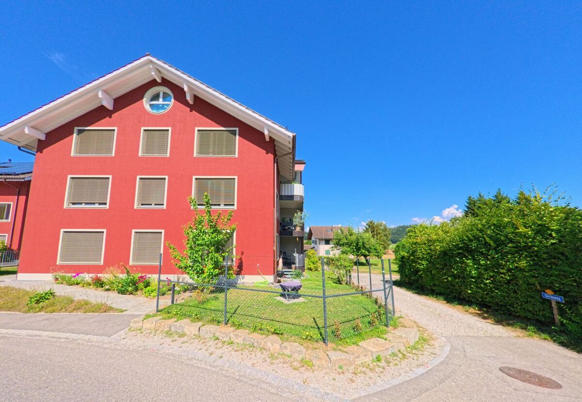 In Thurnen (3127, Kanton Bern) steht ein modernes Mehrfamilienhaus mit roter Fassade an einer Weggabelung, von der ein Kiesweg mit dem Schild „Schmittegässli“ abzweigt.
