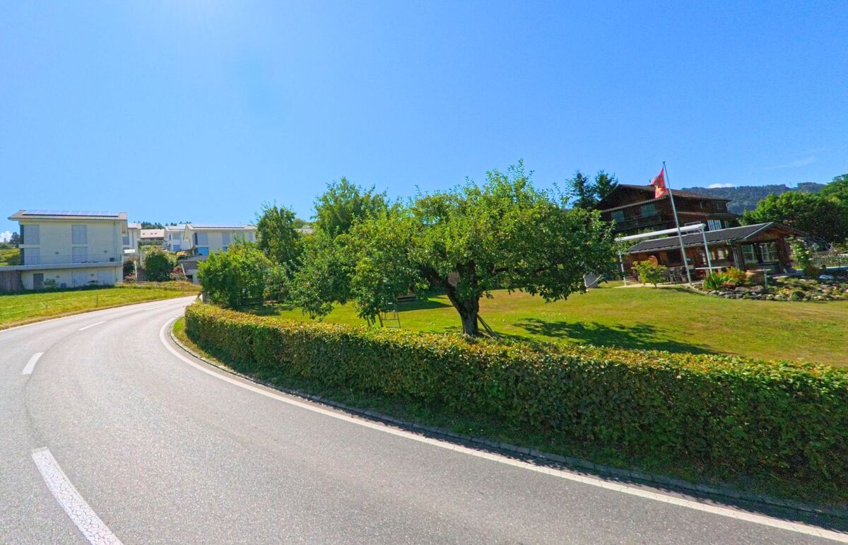 In Thurnen (3128, Kanton Bern) windet sich eine Landstrasse durch eine sonnige Siedlung mit Einfamilienhäusern, gepflegten Gärten und einzelnen Obstbäumen.