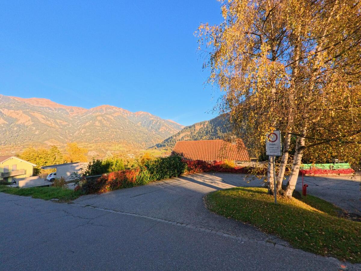 An einer ruhigen Abzweigung öffnet sich in Thusis (7430, Kanton Graubünden) der Blick über herbstlich gefärbte Gärten zu einem Gehöft und den sonnenbeschienenen Berghängen im Hintergrund.