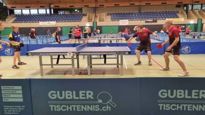 In einer Sporthalle in Zofingen (4800, Kanton Aargau) spielen mehrere Personen ein Tischtennisturnier an parallel aufgestellten Tischen.