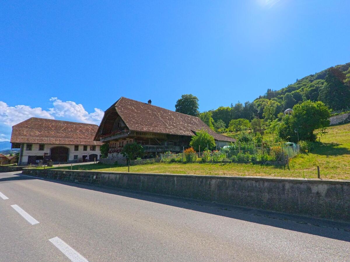 Zwei historische Bauernhäuser mit grossen Walmdächern stehen in Toffen (PLZ 3125, Kanton Bern) an einer Hauptstrasse unterhalb eines bewaldeten Hügels.