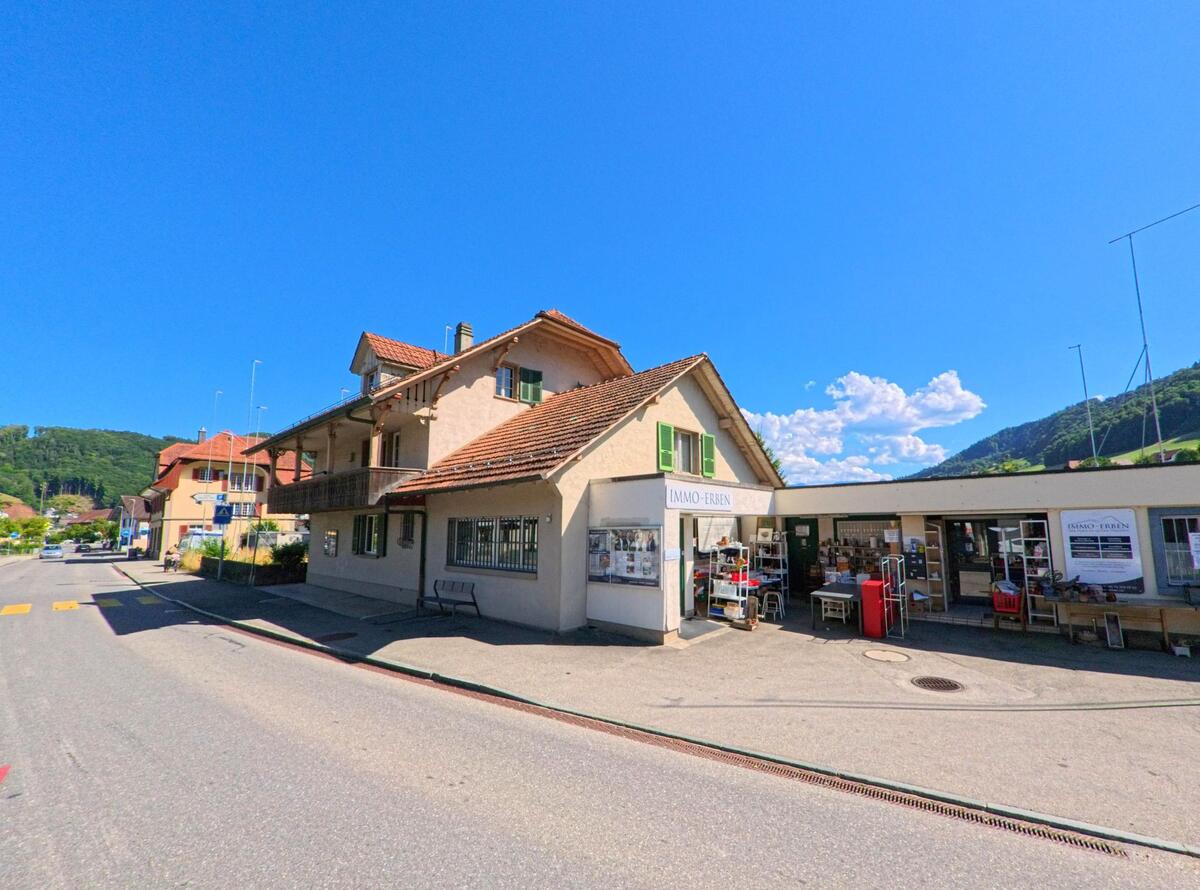 Entlang der Hauptstrasse in Toffen (PLZ 3125, Kanton Bern) befindet sich ein kleines Geschäft mit Schaufenstern und Verkaufsständen, daneben ein Wohnhaus mit Balkon und Ziegeldach.