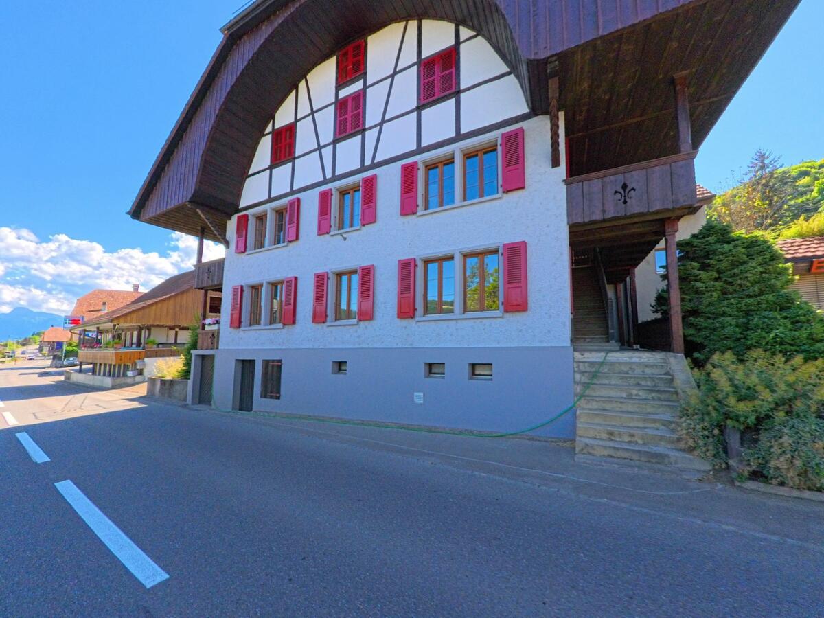 Ein charakteristisches Wohnhaus mit rotem Fensterladen und grossem Vordach steht in Toffen (3125, Kanton Bern) direkt an einer Durchgangsstrasse mit angrenzenden Gebäuden.