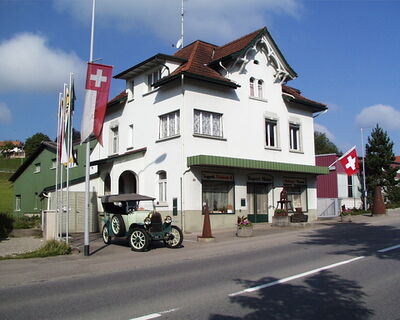 Das Toggenburger Schmiede- und Werkzeugmuseum in Bazenheid (9602, Kanton St. Gallen) befindet sich in einem traditionellen Gebaeude mit Oldtimer vor dem Eingang.