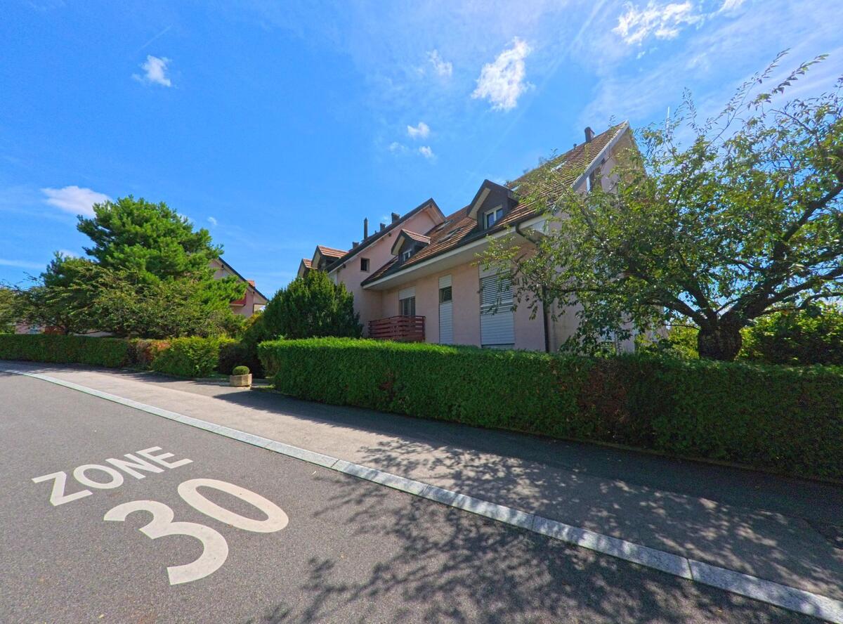 In einer Tempo-30-Zone in Tolochenaz (1131, Kanton Waadt) stehen gepflegte Wohnhaeuser hinter dichten Hecken und Baumen.