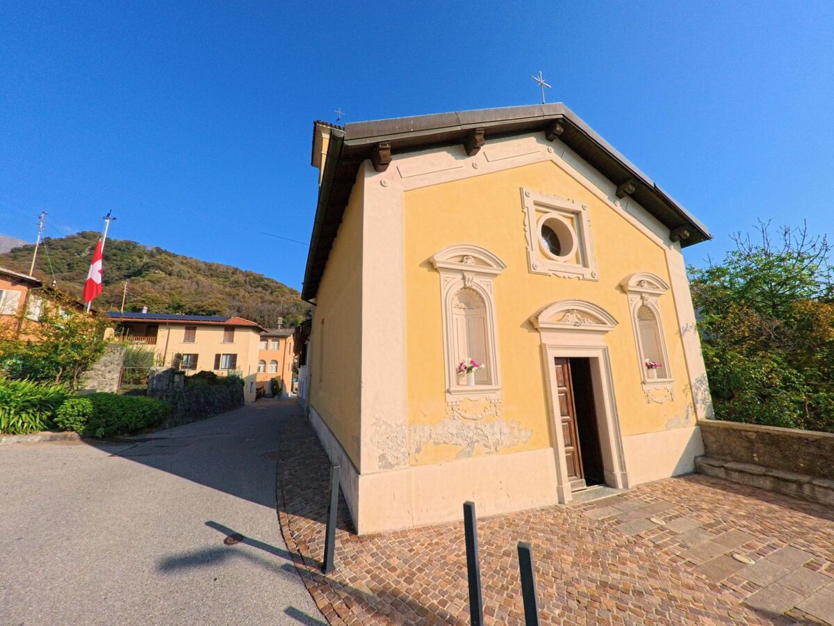 Die kleine Kapelle mit schlichtem Eingang steht in Torricella-Taverne (6908, Kanton Tessin) an einem gepflasterten Weg vor bewaldeten Hügeln.