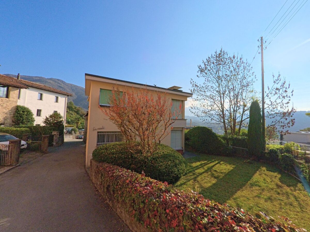 Ein freistehendes Wohnhaus mit gepflegtem Garten liegt in Torricella-Taverne (6908, Kanton Tessin) an einer ruhigen Quartierstrasse vor hügeliger Landschaft.