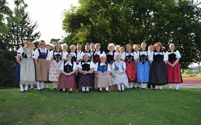 Auf einer Wiese vor grossen Baeumen steht eine Gruppe in traditioneller Trachtenkleidung fuer ein Gruppenfoto in Steffisburg (3114, Kanton Bern).