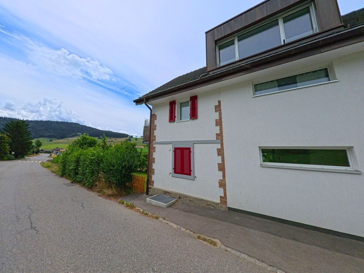 In Treyvaux (1733, Kanton Freiburg) endet eine schmale Wohnstrasse mit Blick auf die umliegenden Hügel und moderne Einfamilienhäuser mit roten Fensterläden.