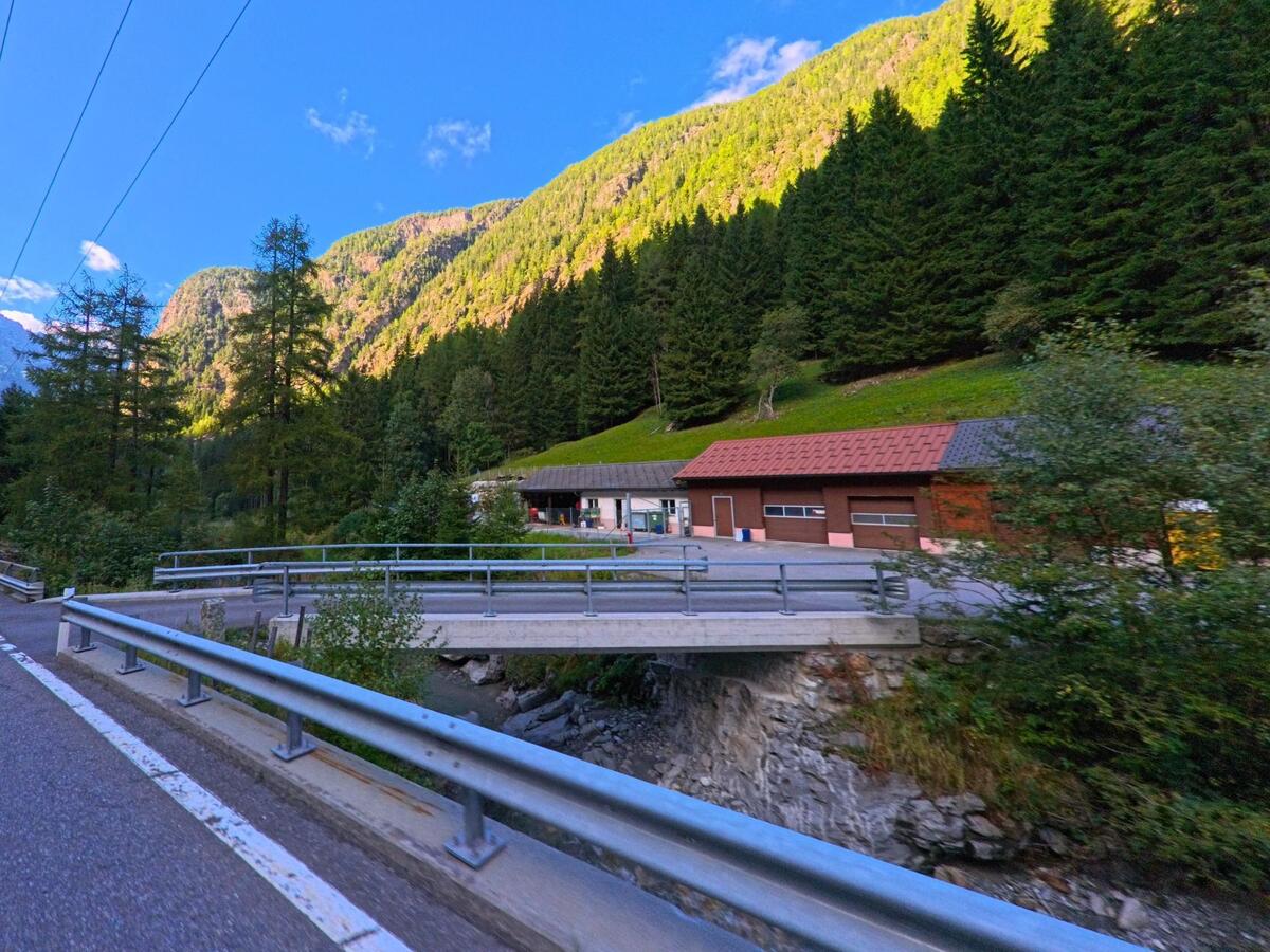 Eine kleine Bruecke fuehrt in Trient (1929, Kanton Wallis) ueber einen Bach zu Gebaeuden, die am Waldrand unterhalb der Berge liegen.