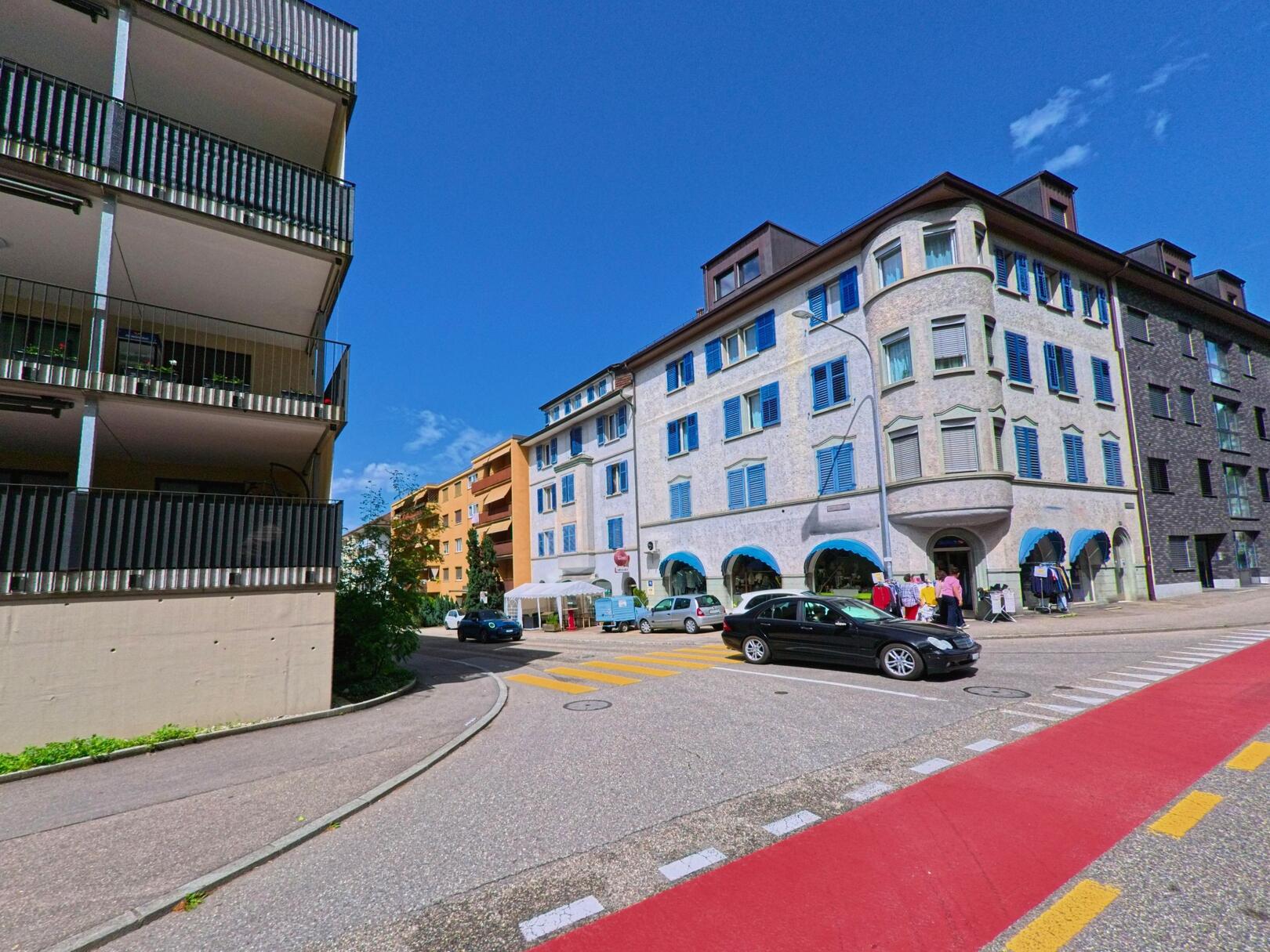 In der Gemeinde Trimbach (4632, Kanton Solothurn) zeigt sich an einer Kreuzung ein Mix aus älteren und modernen Wohn- und Geschäftshäusern bei klarem Sommerhimmel.