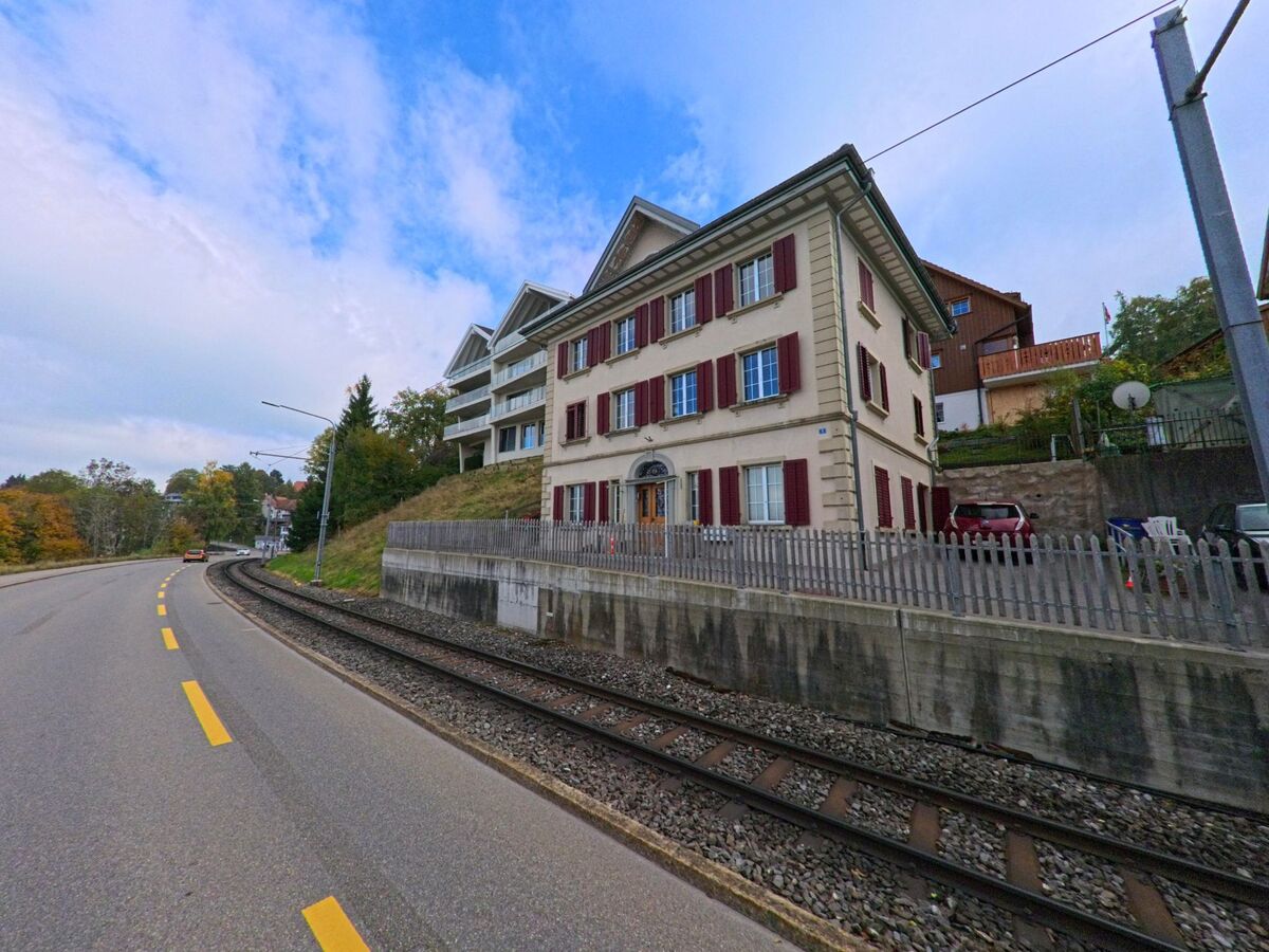 Entlang der Bahnlinie in Trogen (9043, Kanton Appenzell Ausserrhoden) stehen mehrgeschossige Wohnhaeuser mit farbigen Fensterlaeden an einem leicht ansteigenden Hang.