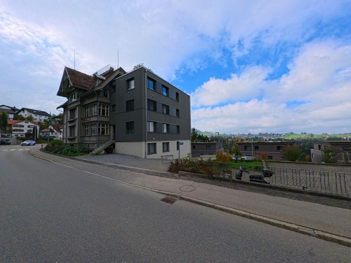 Neben einem modernen Anbau steht in Trogen (9043, Kanton Appenzell Ausserrhoden) ein reich verziertes Holzhaus oberhalb der weiten, huegeligen Landschaft.