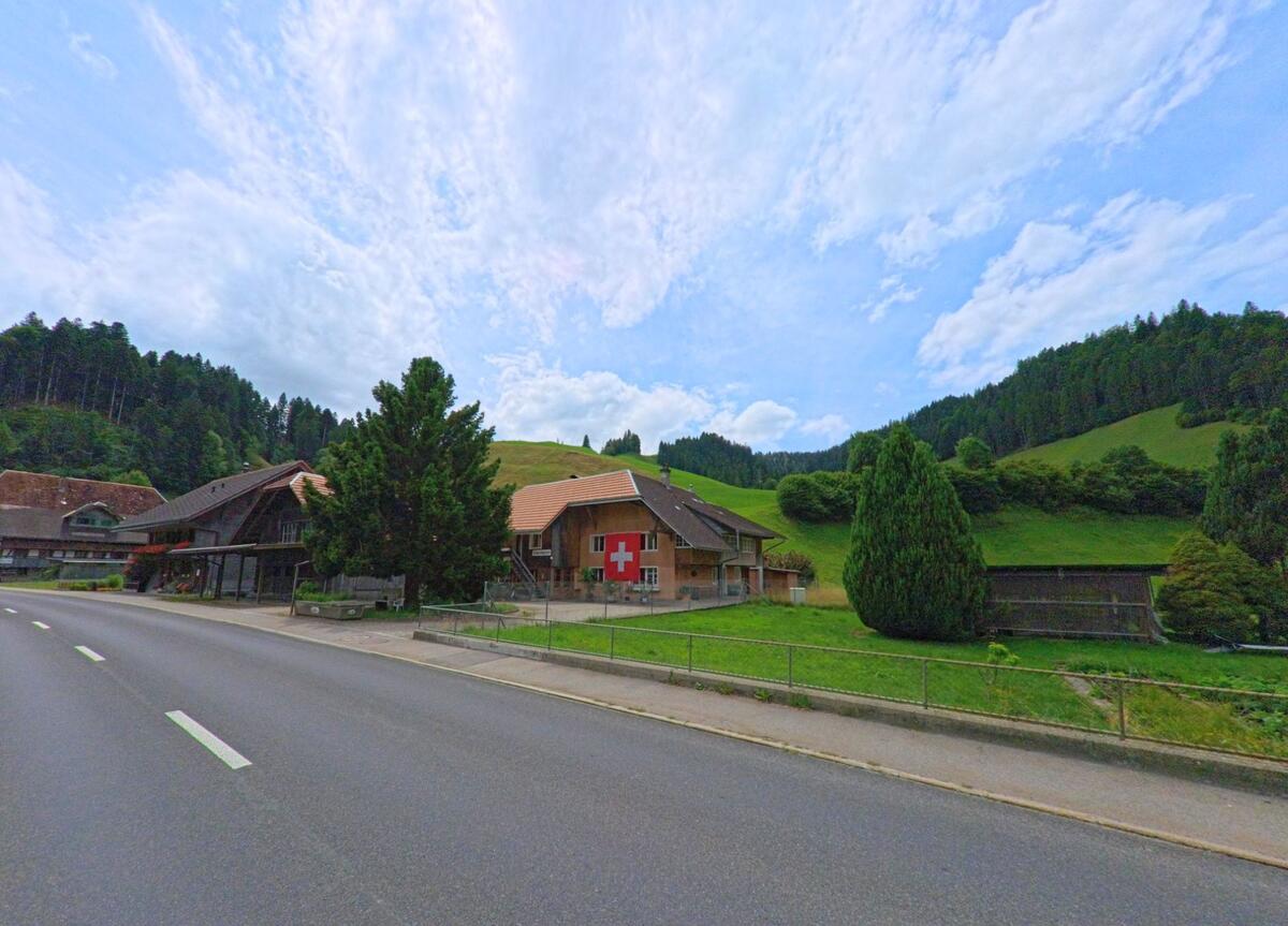 Ein Haus mit grosser Schweizer Fahne an der Fassade steht in Trubschachen (3555, Kanton Bern) idyllisch zwischen grünen Hügeln und Wäldern direkt an der Hauptstrasse.