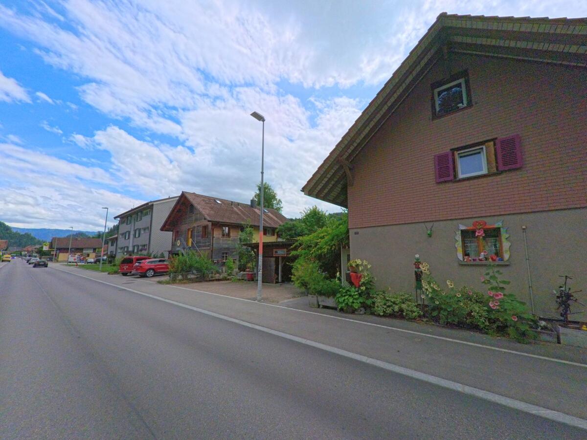 An der Hauptstrasse in Trubschachen (3555, Kanton Bern) stehen Ein- und Mehrfamilienhäuser mit gepflegten Vorgärten, darunter auch ein liebevoll geschmücktes Fenster mit Blumen.