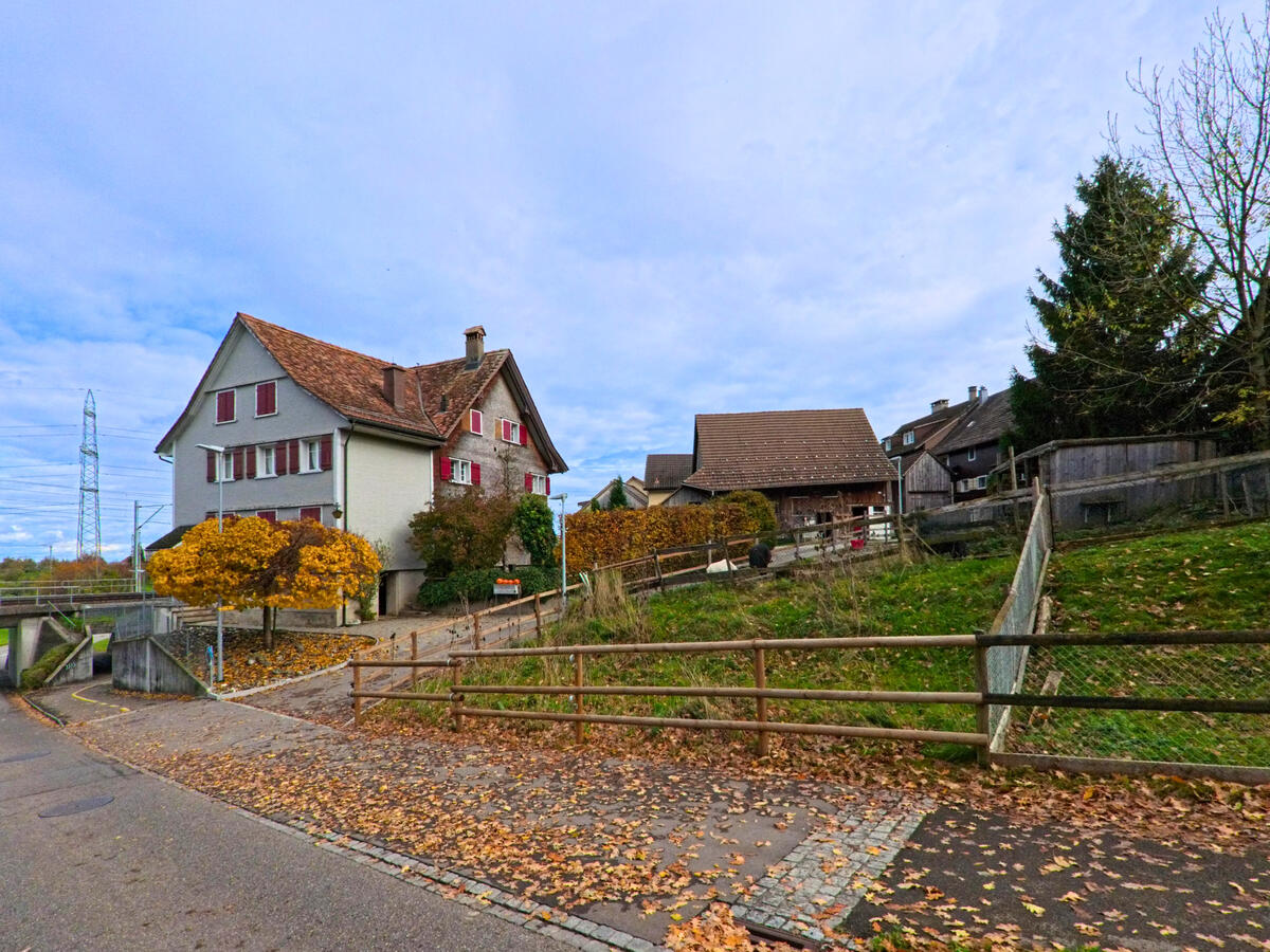 Mehrere Wohnhäuser liegen leicht erhöht an einer Nebenstrasse in Tübach (9327, Kanton St. Gallen) mit Blick über das Quartier.