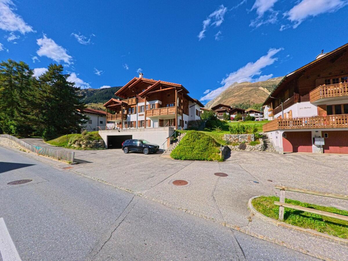 Mehrere Chalets mit Holzbalkonen liegen in Tujetsch (7188, Kanton Graubuenden) an einem sonnigen Hang mit Blick auf die Berge.