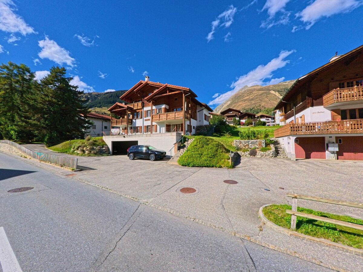 Mehrere Chalets mit Holzbalkonen liegen in Tujetsch (7188, Kanton Graubuenden) an einem sonnigen Hang mit Blick auf die Berge.
