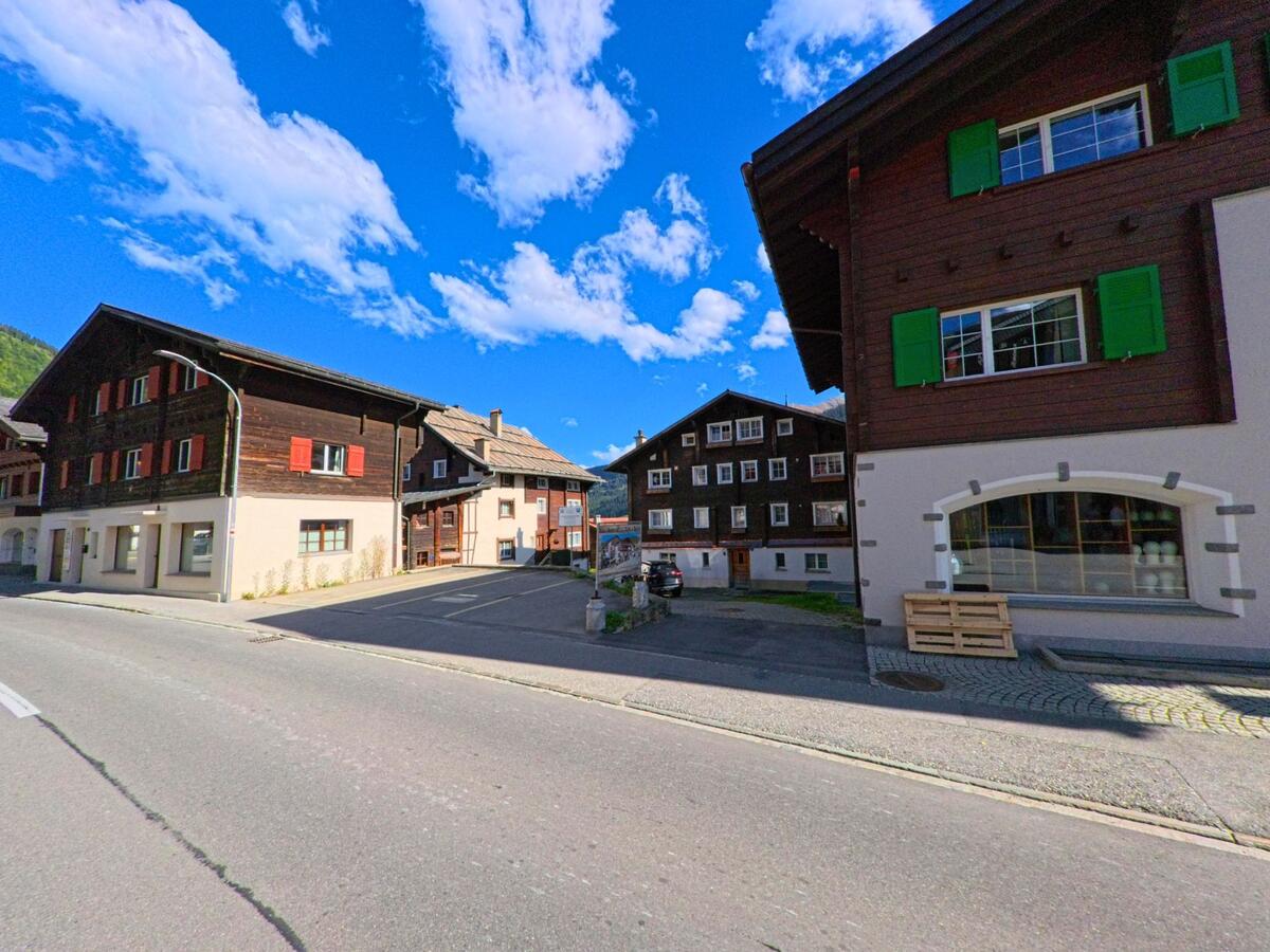 Mehrere traditionelle Holzhäuser mit farbigen Fensterläden stehen in Tujetsch (7188, Kanton Graubuenden) entlang einer ruhigen Strasse im Dorfzentrum.