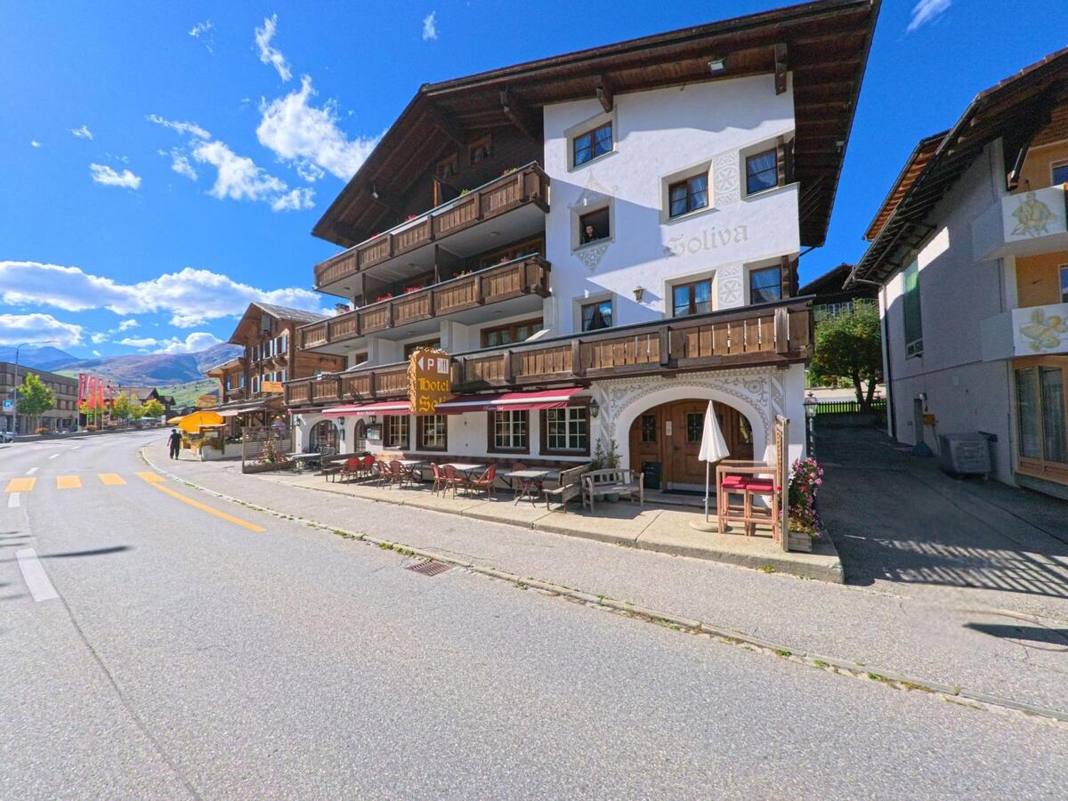Das Hotel Soliva in Tujetsch (7188, Kanton Graubuenden) steht an der Hauptstrasse und besitzt Balkone mit Holzgeländern sowie eine Terrasse mit Sitzplätzen.