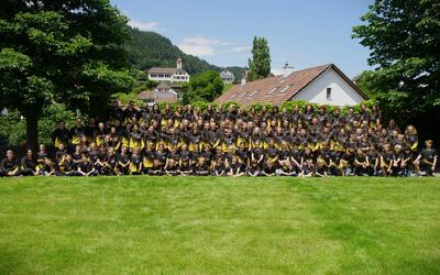 Gruppenbild der Turnvereine Oberschan in 9479 Malans (Kanton Graubünden) auf einer Wiese vor Dorf und Hügeln.