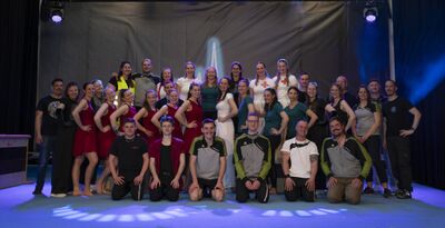 In Moosleerau (5054, Kanton Aargau) posiert der TV/DTV Schmiedrued als grosse bunte Gruppe auf einer Bühne unter Scheinwerfern für ein gemeinsames Foto.