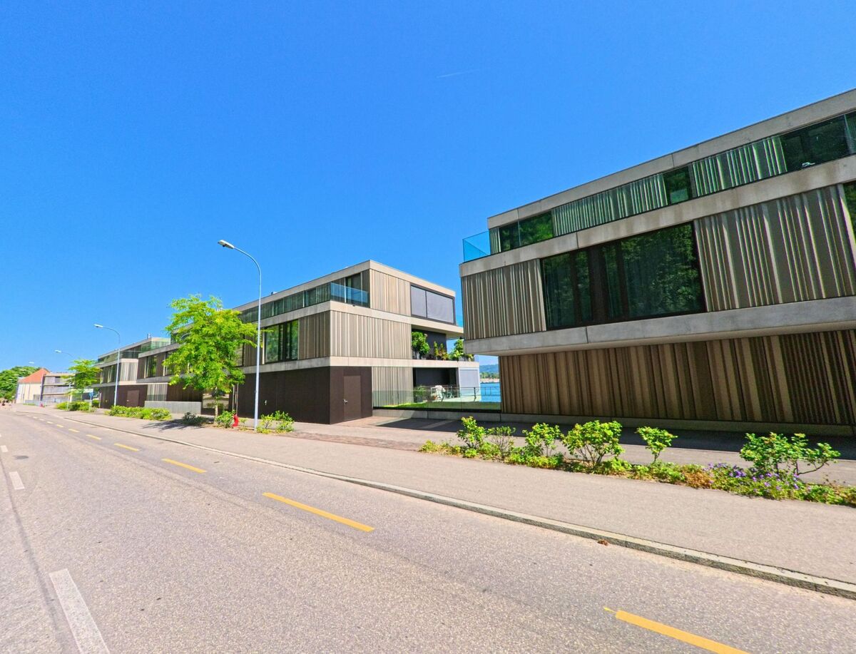 In Twann (2505, Kanton Bern) zeigt sich eine moderne Wohnanlage entlang der Straße, umgeben von grünen Bepflanzungen und bei strahlendem Sonnenschein.