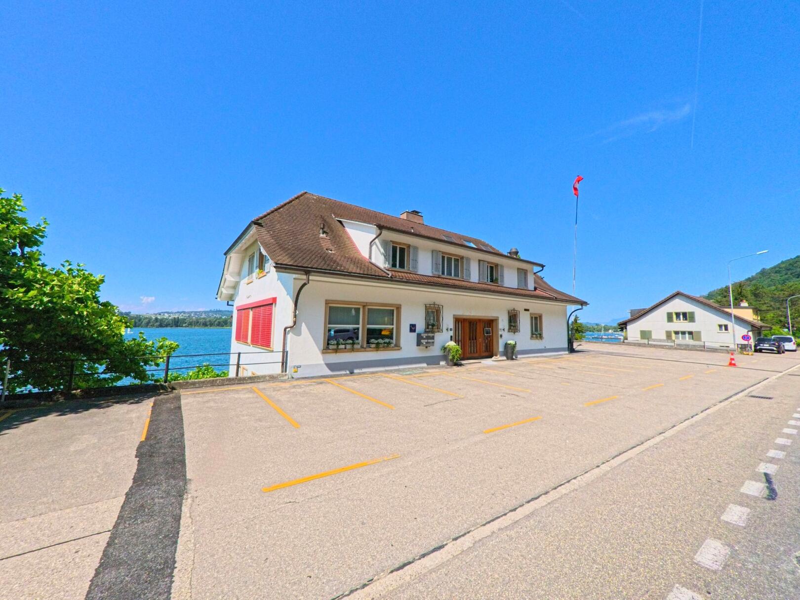 In Twann (2505, Kanton Bern) befindet sich ein Restaurant direkt am See, umgeben von grünen Bäumen und mit einem klaren Blick auf das Wasser, bei strahlendem Sonnenschein.