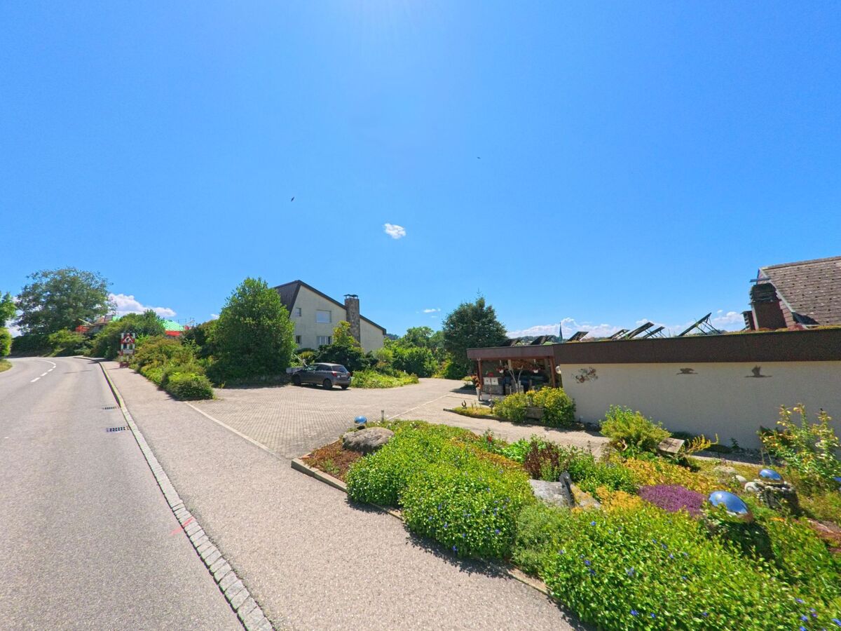 An einer leicht kurvigen Strasse in Ueberstorf (3182, Kanton Freiburg) befindet sich ein Haus mit grossem Vorplatz und gepflegtem Steingarten.