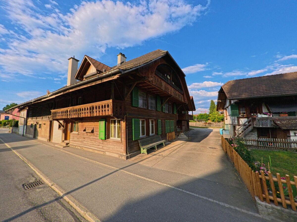 Zwei traditionelle Bauernhäuser mit Holzfassaden und grünen Fensterläden stehen sich in einer schmalen Gasse in Uetendorf (3661, Kanton Bern) gegenüber.