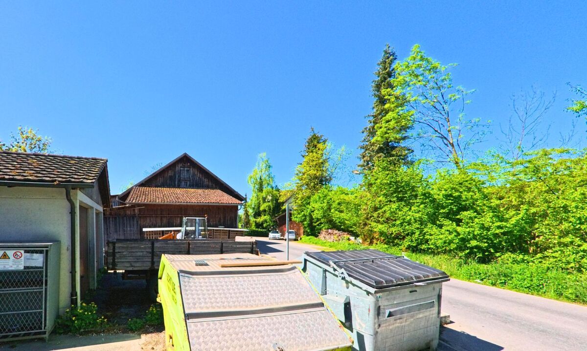 In Uetikon am See (8707, Kanton Zürich) stehen Container und Sammelstellen am Rand einer schmalen Strasse neben einem alten Holzgebäude.