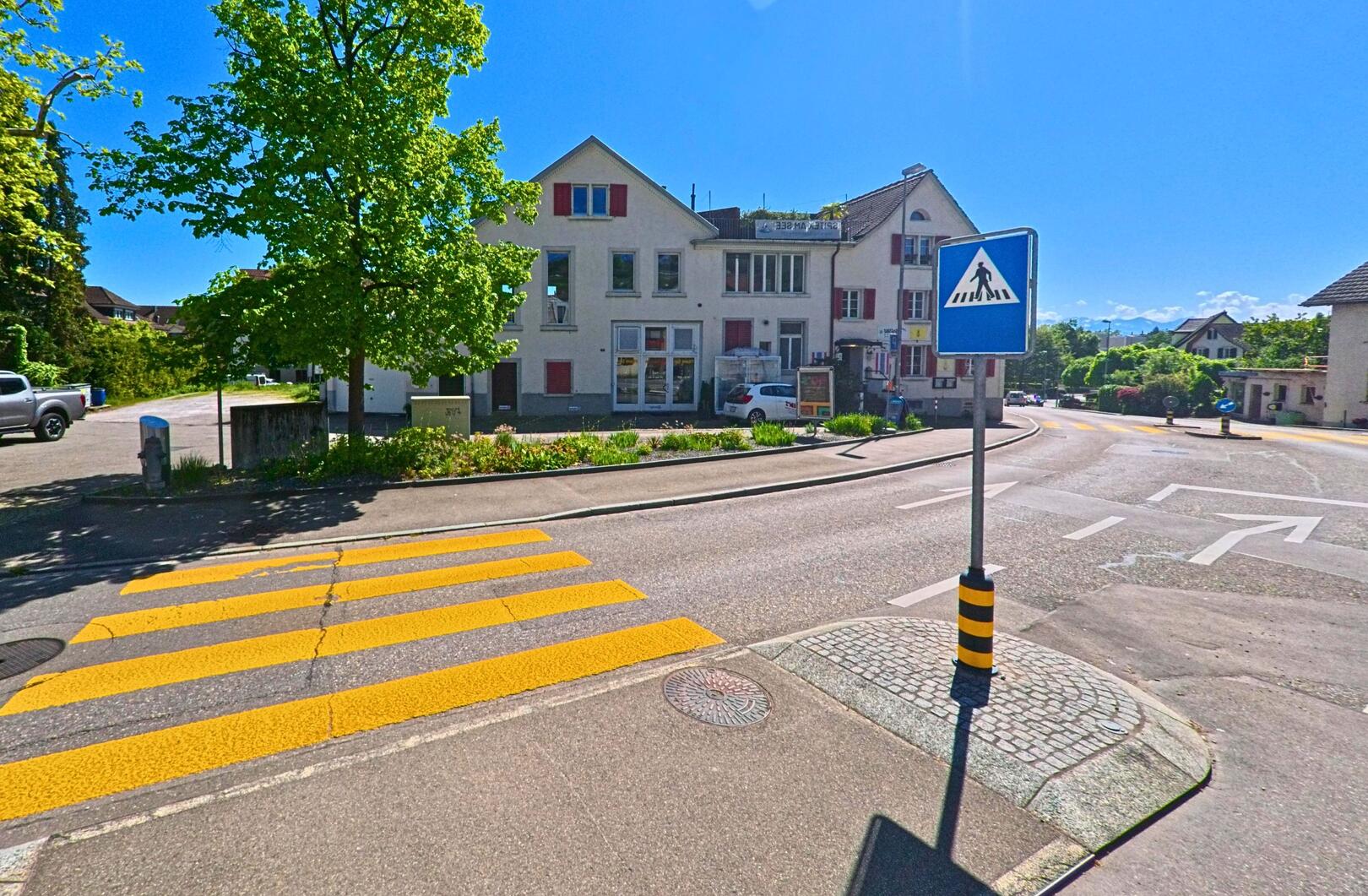 An einer gut sichtbaren Kreuzung in Uetikon am See (8707, Kanton Zürich) führen Wegweiser zum Gemeindehaus und zur Kantonsschule, während ein Zebrastreifen die Fahrbahn markiert.