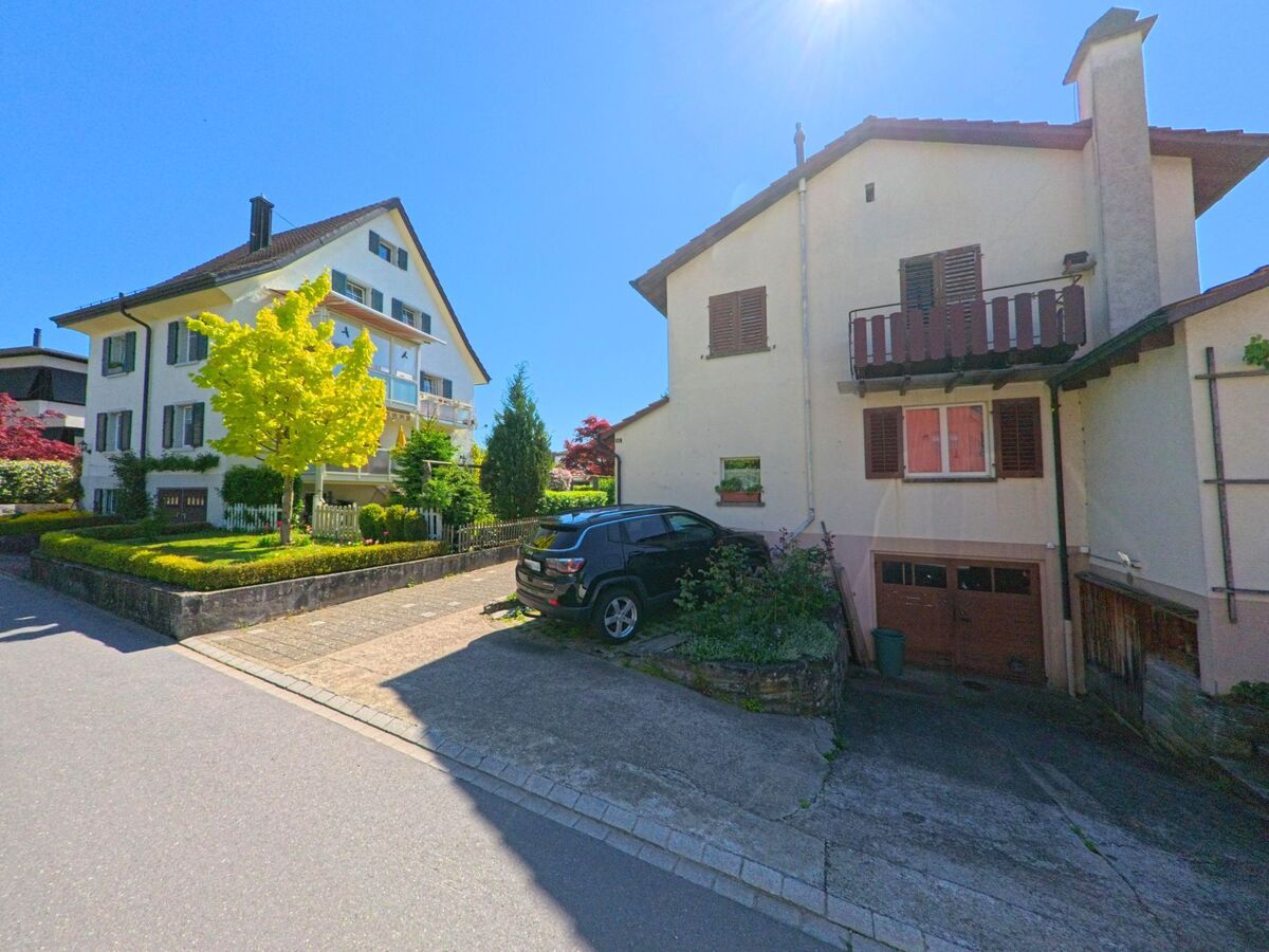  In einem Wohnquartier von Uetikon am See (8707, Kanton Zürich) stehen zwei gepflegte Einfamilienhäuser mit Vorgärten und Garagen bei strahlendem Sonnenschein nebeneinander.