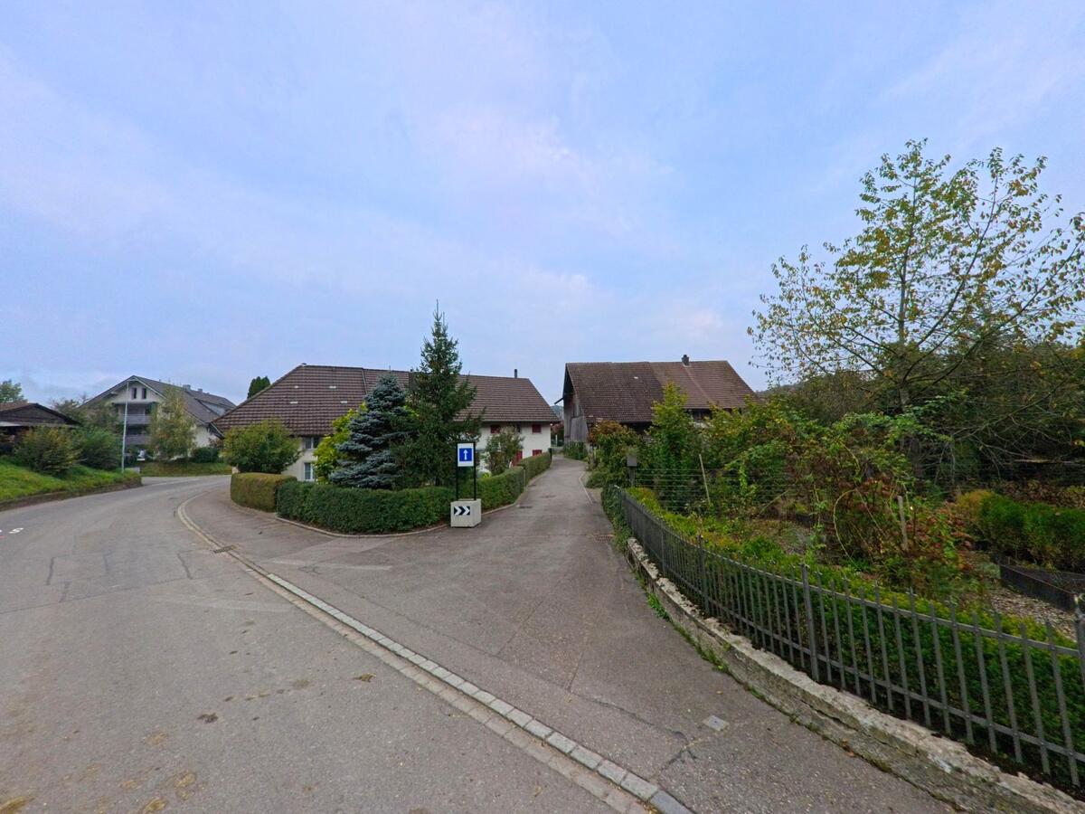 In Uezwil (5619, Kanton Aargau) zweigt eine schmale Sackgasse von einer gekruemmten Wohnstrasse ab, umgeben von Einfamilienhaeusern und dichter Bepflanzung.