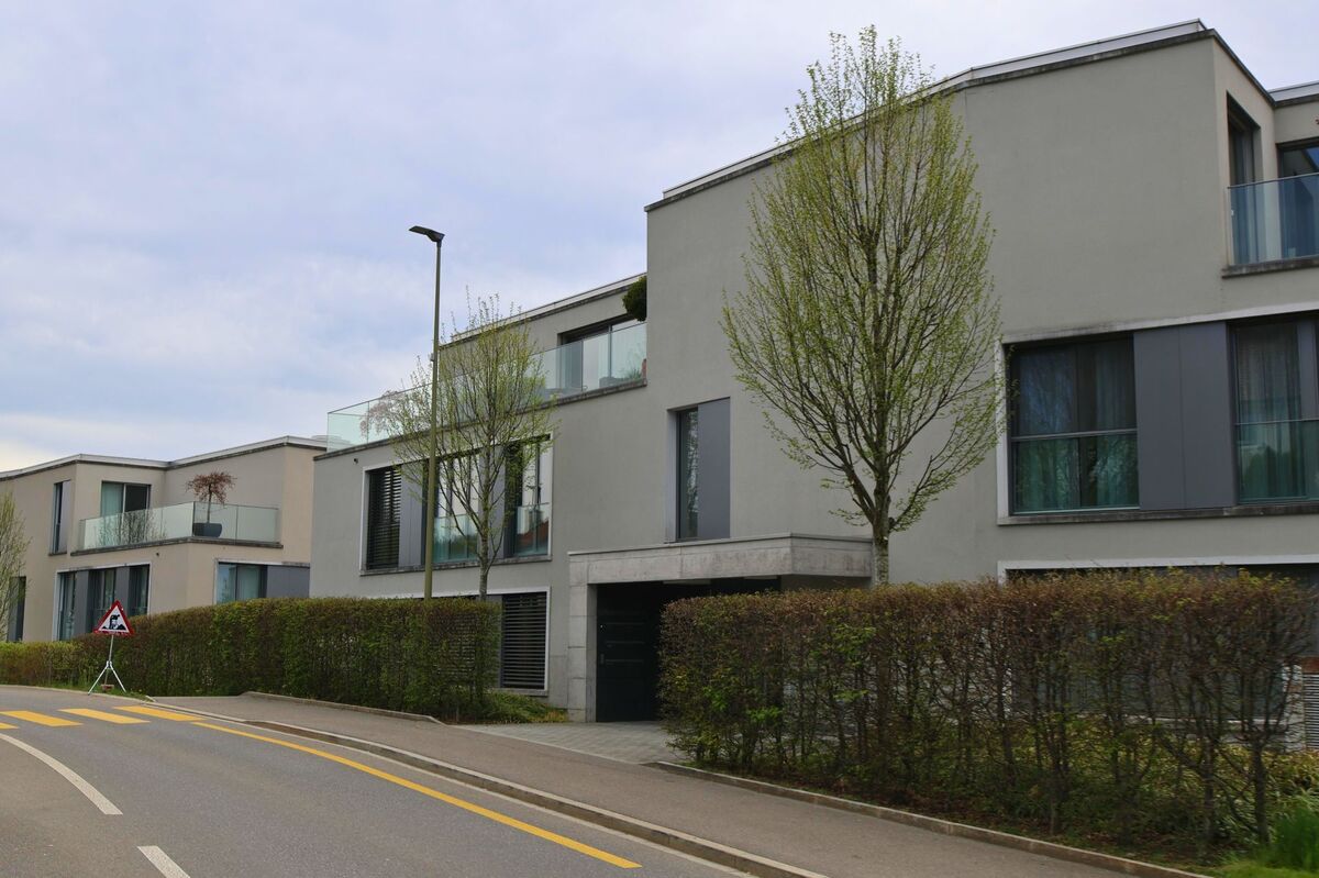 Moderne Wohngebäude mit grossen Glasbalkonen säumen in Uitikon (8142, Kanton Zürich) eine Strasse mit frisch markierten gelben Fussgängerstreifen.