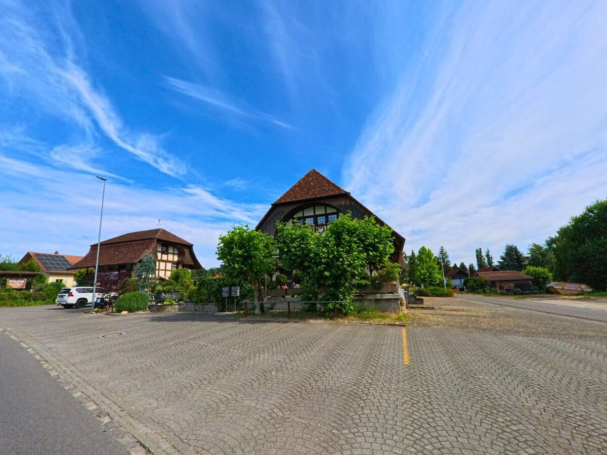 In Ulmiz (3214, Kanton Freiburg) stehen mehrere traditionelle Gebäude mit steilen Dächern an einem grosszügig gepflasterten Platz.