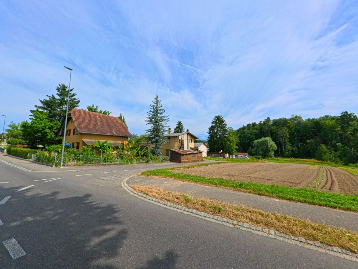 Am Übergang zwischen Siedlung und Landwirtschaftsfläche in Ulmiz (3214, Kanton Freiburg) liegen Einfamilienhäuser direkt neben einem frisch bestellten Feld.