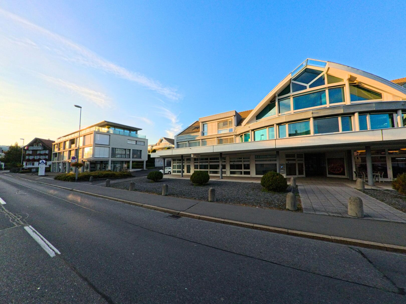 In Unteraegeri (6314, Kanton Zug) zeigt das Bild moderne Gebaeude entlang einer breiten Strasse, die im Abendlicht klar strukturiert wirkt.