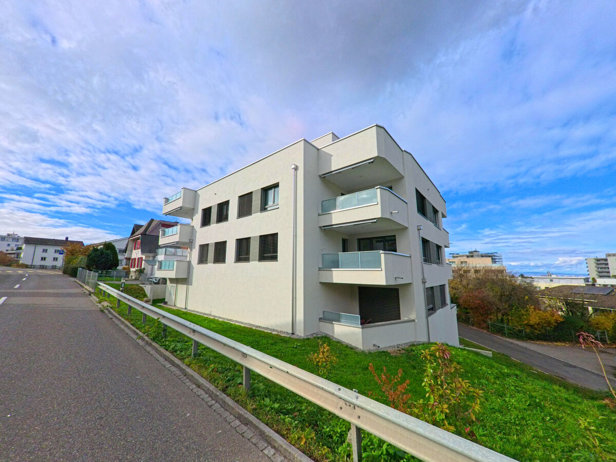 Ein modernes Wohngebaeude mit Balkonen liegt oberhalb der Fahrbahn in Untereggen (9303, Kanton St. Gallen).