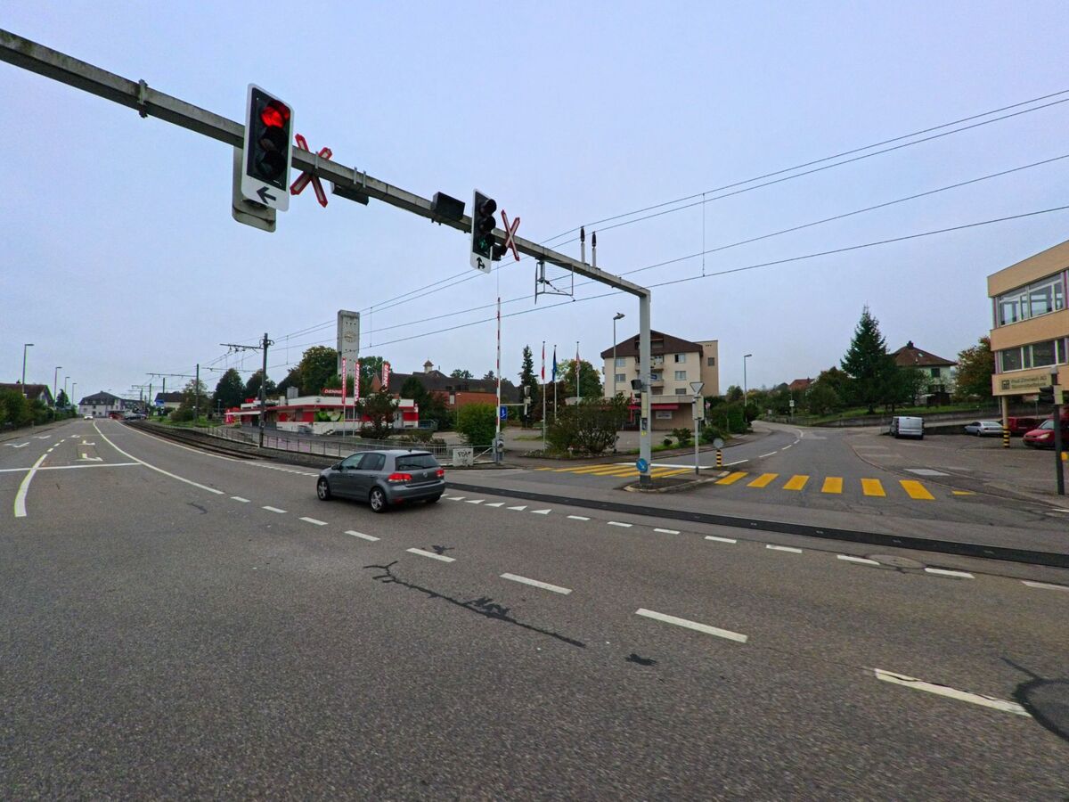Eine befahrene Kreuzung in Unterentfelden (5035, Kanton Aargau) zeigt eine Ampelanlage ueber den Tramgleisen sowie einen gelb markierten Fussgaengerstreifen.