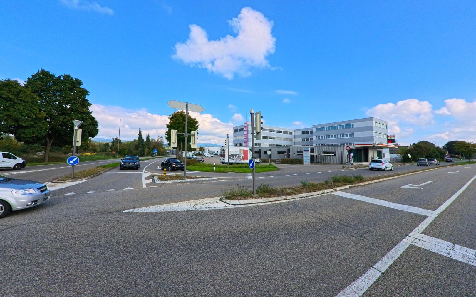 In Unterentfelden (5035, Kanton Aargau) zeigt das Bild eine breite Strassenkreuzung mit Verkehrsinseln, umgeben von Baeumen und modernen Gebaeuden.