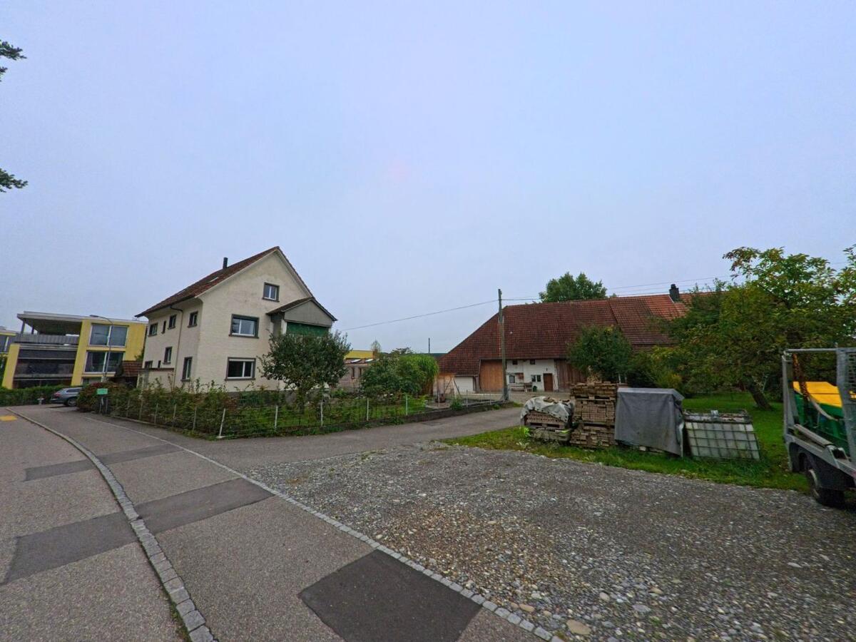 In Unterentfelden (5035, Kanton Aargau) liegt ein kleines Wohnquartier mit einem schlichten Einfamilienhaus und einer angrenzenden Scheune an einer ruhigen Strasse.