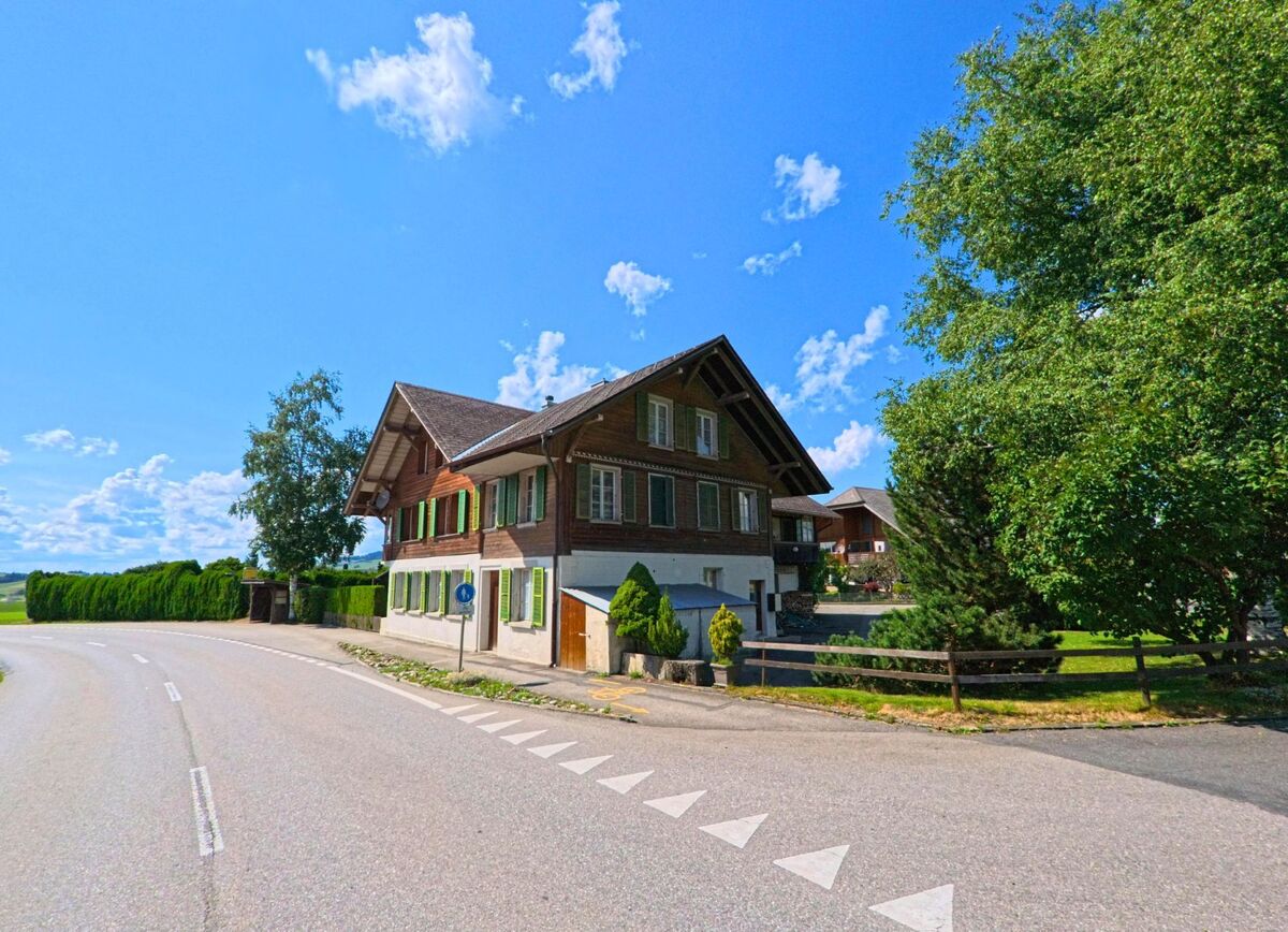 Am Rand einer sanft geschwungenen Strasse in Unterlangenegg (3614 im Kanton Bern) steht ein gepflegtes Wohnhaus mit gruenen Fensterlaeden und Vorgarten.