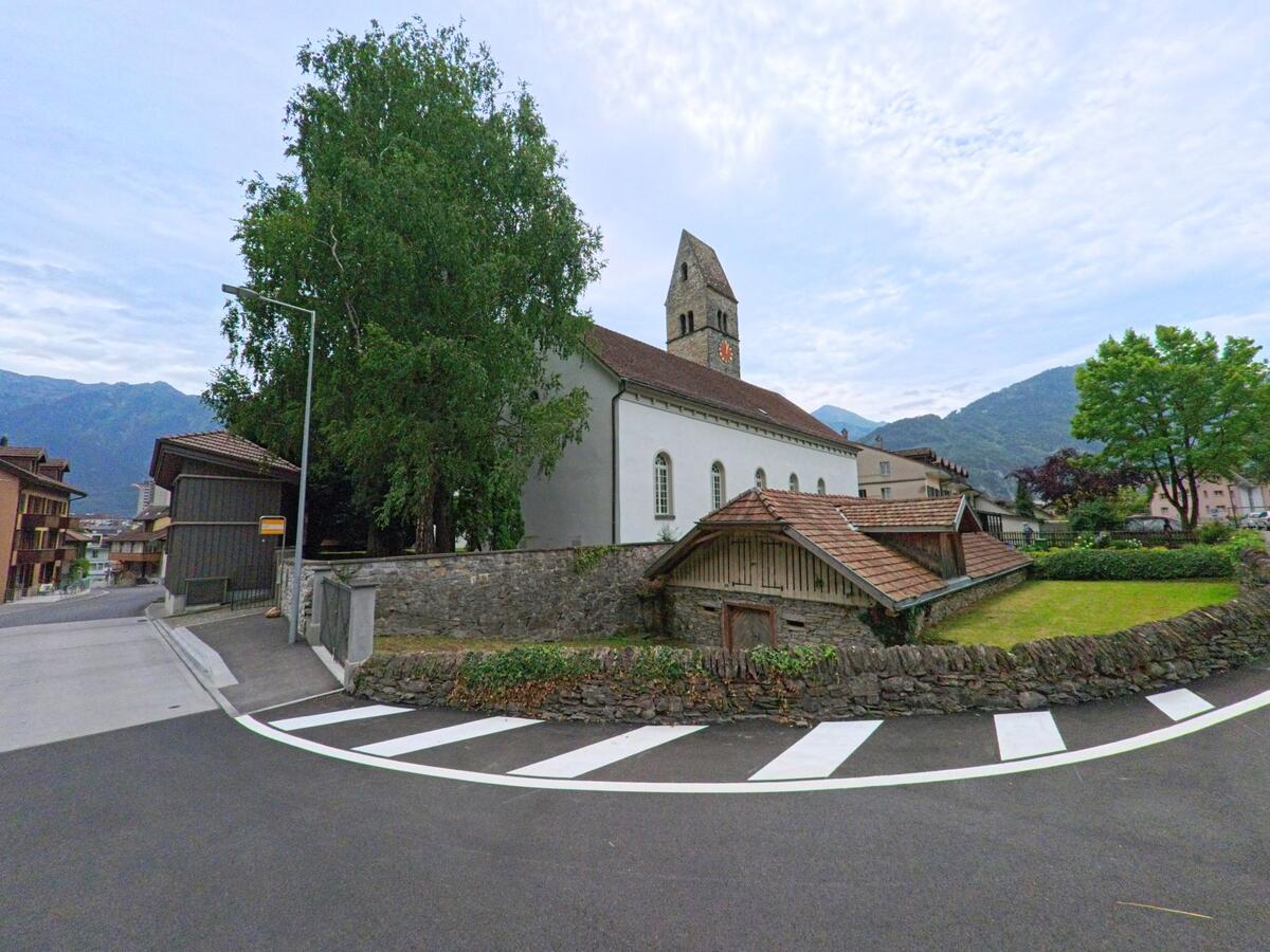 Die Kirche von Unterseen (3800, Kanton Bern) steht mit ihrem markanten Turm und Uhr vor den bewaldeten Bergen des Berner Oberlands.