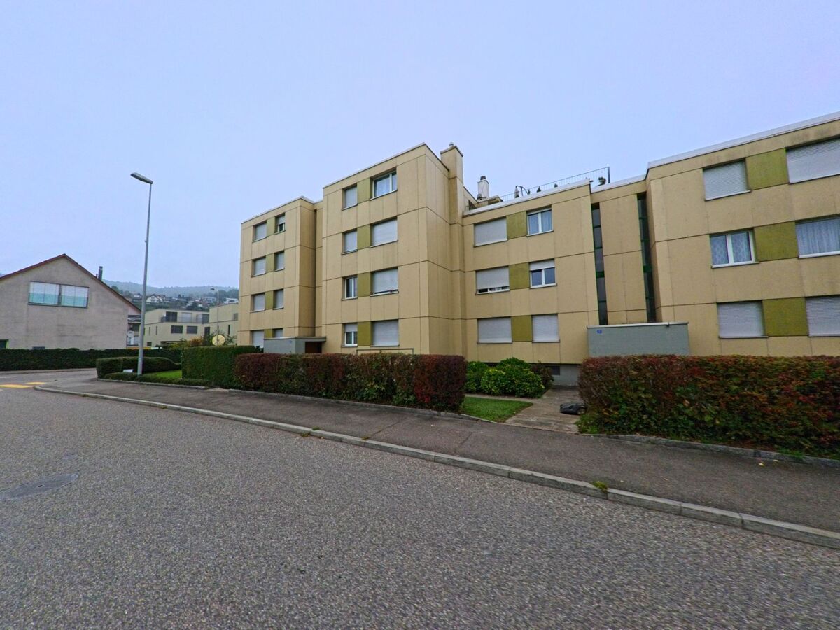 Mehrere zusammenhängende Mehrfamilienhäuser mit gepflegten Grünflächen säumen eine ruhige Quartierstrasse in Untersiggenthal (5417, Kanton Aargau) bei bedecktem Himmel.