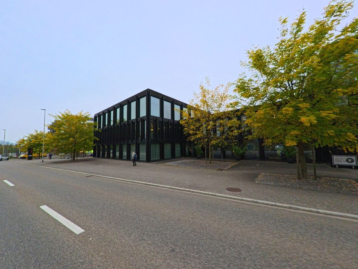 Ein markantes, modernes Gebäude mit dunkler Fassade und grossen Glasflächen steht an einer breiten Strasse in Untersiggenthal (5417, Kanton Aargau), umgeben von herbstlich gefärbten Bäumen.