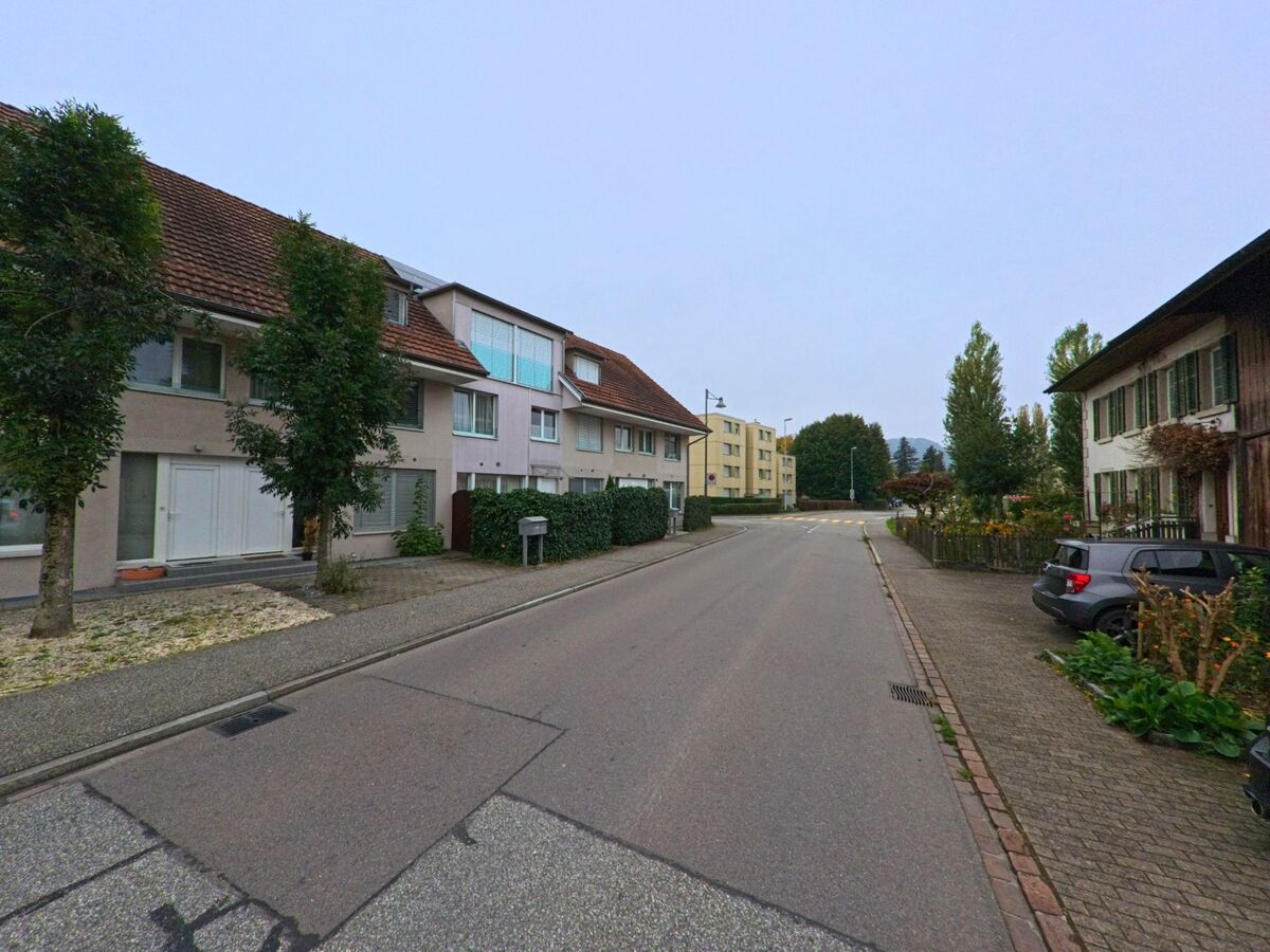 In einer ruhigen Wohnstrasse mit gepflegten Häusern und Gärten in Untersiggenthal (5417, Kanton Aargau) stehen Bäume entlang des Gehwegs, während die Strasse sich sanft biegt.