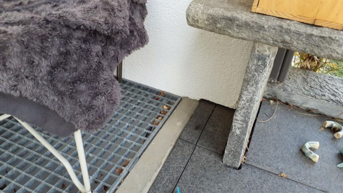  In Urdorf (PLZ 8902, Kanton Zürich) ist ein Teil eines Aussenbereichs mit einem Gitterrost, einem Stuhl und einigen verstreuten Objekten zu sehen.