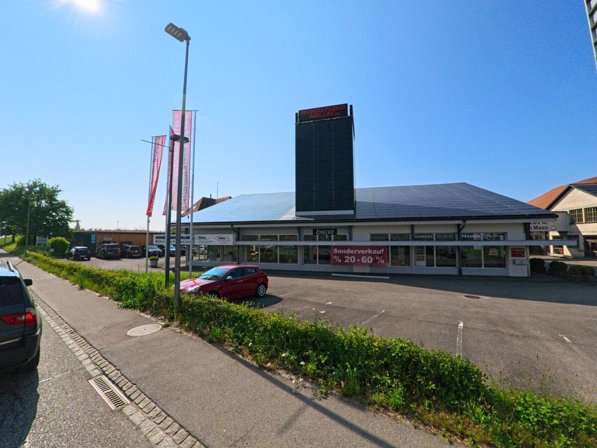 Ein grossflächiges Geschäftsgebäude mit vorgelagertem Parkplatz und Leuchtturm steht an einer verkehrsnahen Lage in Urtenen-Schönbühl (3322, Kanton Bern) unter klarem Himmel.